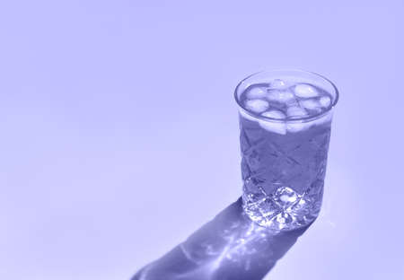 Beautiful crystal glass casts long shadow from sunlight. Toned in trendy color of year 2022. Minimal creative composition with copy space. Summer drinks concept.の写真素材