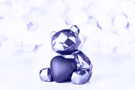 Gift card with chocolate bear holding heart on background of christmas lights bokeh. Toned in trendy...