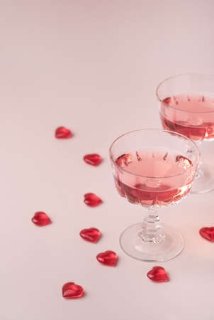 Two crystal glasses of rose sparkling wine or champagne and red glass hearts on pastel pink background. Happy Valentines Day concept. Minimal creative composition with copy space.の写真素材