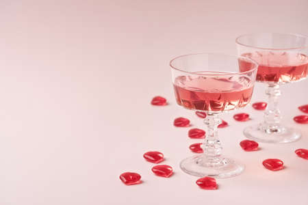 Two crystal glasses of rose sparkling wine or champagne and red glass hearts on pastel pink...