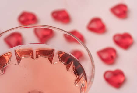 Crystal glass of rose sparkling wine or champagne and red glass hearts on pastel pink background. Shot with selective soft focus. Happy Valentines Day concept.の写真素材
