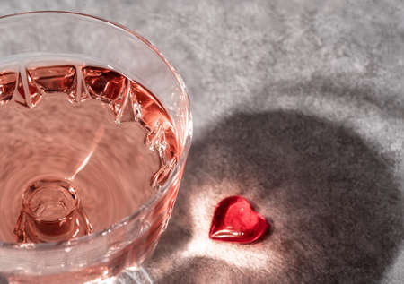 Top view of crystal glass of rose sparkling wine or champagne and red glass heart on grey stone background in hard light with shadows. Happy Valentines Day concept.の写真素材