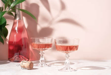 Two crystal glasses of rose sparkling wine or champagne on pastel pink marble table in sunlight. Minimal creative composition with copy space. Summer drink concept.の写真素材