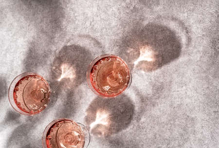 Top view of three crystal glasses of rose sparkling wine or champagne on grey stone background in...