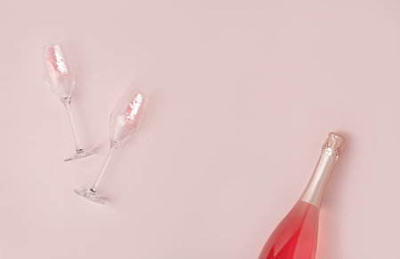 Creative trendy flat lay with pink champagne bottle and flutes filled with pink heart shaped confetti on pastel background. Flat lay, copy space. Holiday concept.の写真素材