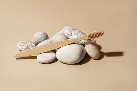 Organic wooden bamboo toothbrush and white sea pebbles on beige background. Natural beauty and...