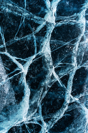 Transparent dark blue ice of frozen Baikal lake with white cracks pattern. Beautiful winter nature background.の写真素材