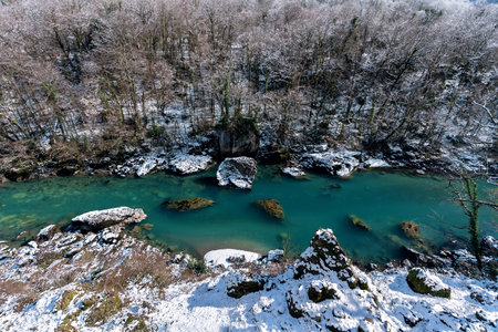 Beautiful winter landscape with emerald mountain river with snow-covered trees along the shore on a sunny day. Great natural background with copy space for your design.の写真素材