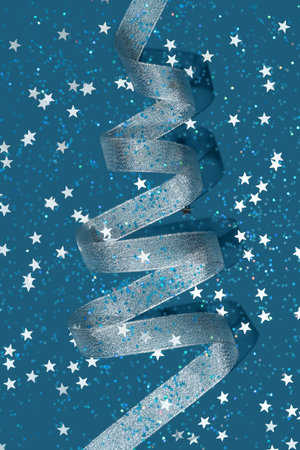 Silver party streamer in the shape of Christmas tree and sparkling star shape confetti on blue background. Holiday concept. Copy space.の写真素材