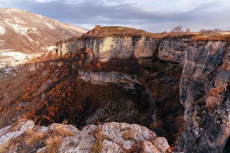 Vibrant autumn colors highlight the rugged cliffs of a deep canyon. The landscape features steep rock faces and scattered trees, creating a breathtaking natural view at sunset.の写真素材