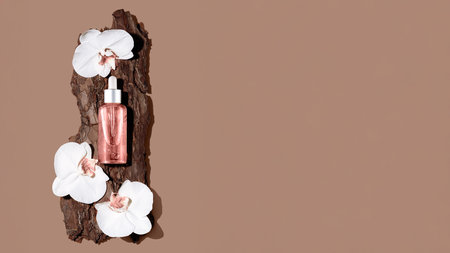 Glossy beauty oil bottle is artistically arranged with white orchid flowers on a piece of textured wood, set against a warm, neutral backdrop, creating an elegant and modern aesthetic.の写真素材