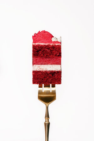 Red velvet cake slice elegantly balanced on a golden fork, revealing vibrant layers of cake and...