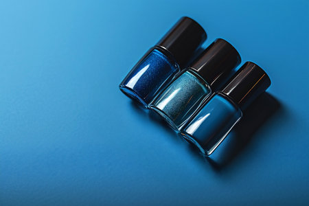 Three blue nail polish bottles are elegantly placed in a flat lay arrangement on a smooth blue surface, providing ample copy space for branding or design elementsの素材