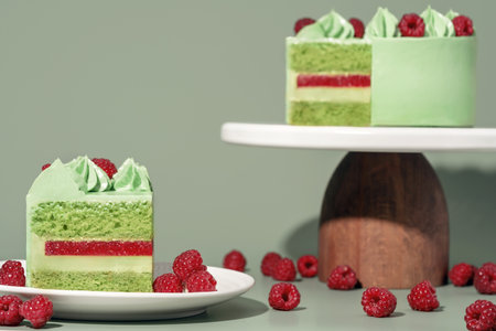 A vibrant pistachio and raspberry cake is elegantly presented on a white cake stand, surrounded by fresh raspberries, creating a delightful bakery concept with ample copy space for menu designの写真素材