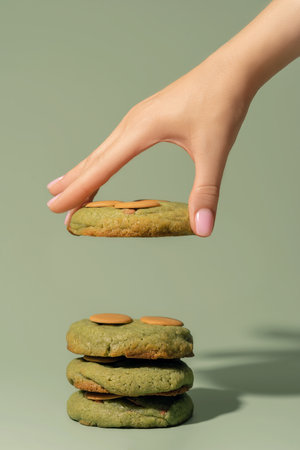 Hand delicately positions a pistachio cookie atop a stack, highlighting the bakery concept with rich textures and colors, perfect for menu design with copy spaceの写真素材