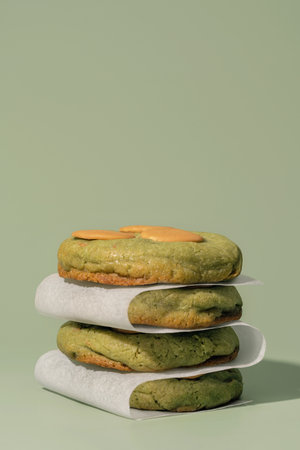 Stacked pistachio cookies with creamy filling on parchment paper, set against a soft green backdrop, ideal for bakery concepts and menu designs with copy spaceの写真素材