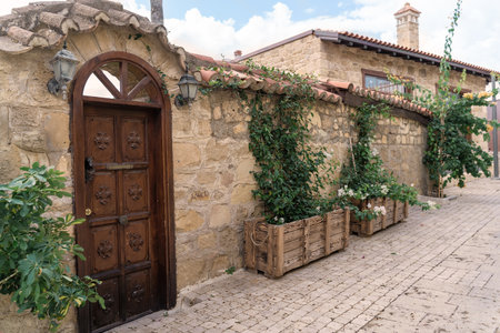 Rustic wooden door set within a textured stone wall, surrounded by vibrant greenery and wooden crates, creating a warm and inviting atmosphere in an outdoor environment filled with natural beautyの写真素材