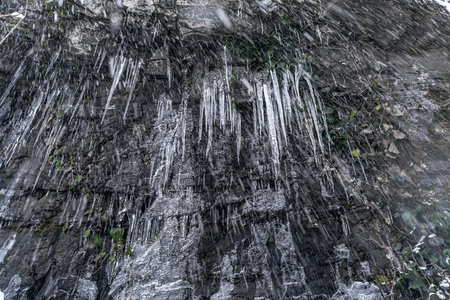Natural rock formation featuring striking icicles and lush greenery, creating a captivating scene with ample copy space for design elements and text integration in various projectsの写真素材