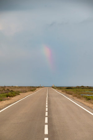 An empty road stretching to the horizon, with a rainbow in the sky, is a reminder of the endless possibilities of life.の写真素材