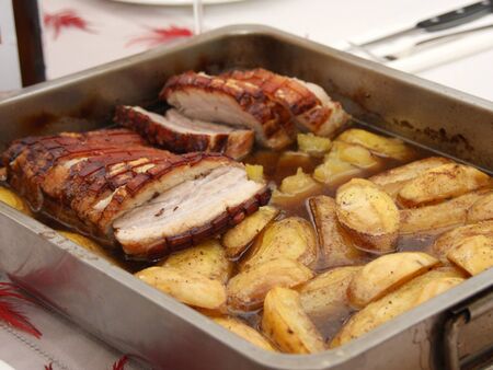 Homemade roast pork belly with fried potatoes sliced ââin juice served in a roasting pan on a set tableの写真素材