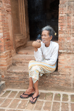 Bagan, Myanmar, March 26, 2014. Asiatic old woman smoking a big handmade cigar in Bagan, Myanmar.のeditorial素材