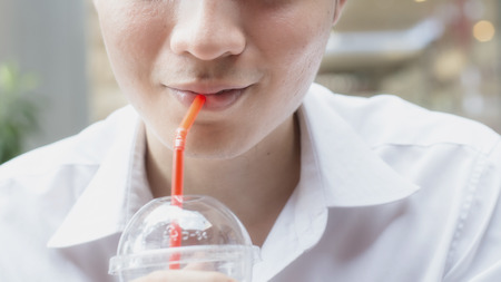 Asian young man using a straw to drink from a plastic cup.の写真素材