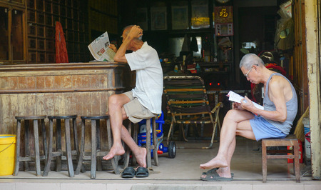 HOI AN - APIRL 18, 2015. Elderly Chinese men reading newspaper in front of his shop, Hoi An, Vietnam.のeditorial素材