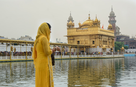 Amritsar, India - Jul 22, 2015. A woman in a yellow saree standing opposite the Golden Temple in Amritsar, India.のeditorial素材