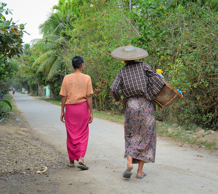 NGAPALI, MYANMAR - JANUARY 18, 2015. Unidentified Burmese women carrying a heavy basket, walking on the street in Ngapali, Myanmar (Burma).のeditorial素材