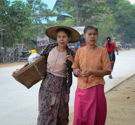 NGAPALI, MYANMAR - JANUARY 18, 2015. Unidentified Burmese women carrying a heavy basket, walking on the street in Ngapali, Myanmar (Burma).のeditorial素材
