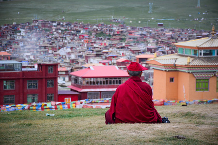 A Tibetan monk sitting on the hill at sunset in Yarchen Gar, Sichuan, China. Yarchen Gar is the largest concentration of nuns and monks in the world.の写真素材