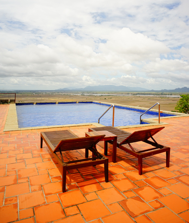 Relaxing chairs at beautiful swimming pool with rice field background in the countryside of southern...