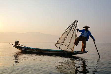 Inle, Myanmar - Feb 14, 2016. A Burmese man using the unique methods of rowing and catching fish on Inle Lake at early morning in Shan State, Myanmar.のeditorial素材