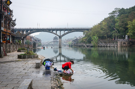 Hunan, China - Nov 6, 2015. Women wash clothes on riverbank at Fenghuang Ancient Town in Hunan, China. Fenghuang is situated at the foot of mountains and beside waters.のeditorial素材