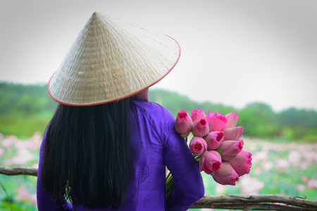 Close-up of Asian woman in traditional dress (Vietnamese Ao Dai) with lotus flower.の写真素材