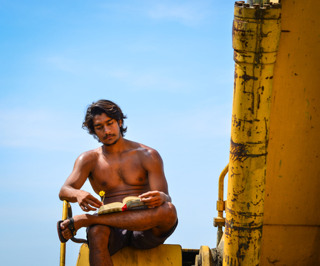 An Indian young worker reading book on the construction machine at sunny dayの写真素材