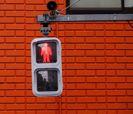 Traffic lights for pedestrian showing the red, with brick wall background.