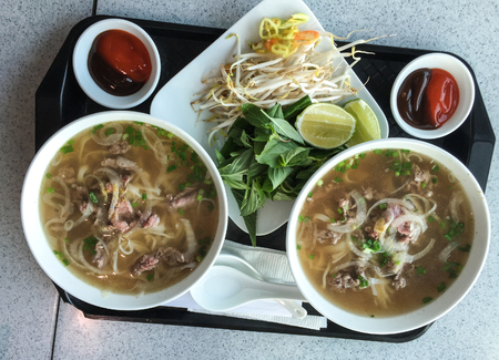Bowl of Vietnamese pho noodle soup with rare beef, tendon, tripe and brisket served with onions, scallions and cilantro.の写真素材