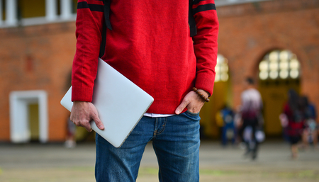 Young student holding a laptop and standing at old college in Dalat, Vietnam.の写真素材