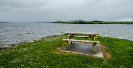 A wooden chair on green hill, looking at the lake.の写真素材