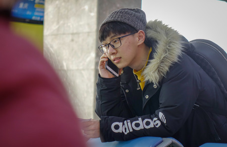Harbin, China - Feb 28, 2018. A teenager taking on cellphone at Departure Terminal of Harbin Airport (HRB), Heilongjiang Province, China.のeditorial素材