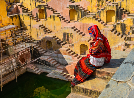 A woman in traditional dress sitting on steps of the ancient Indian deep well in Jaipur, India.