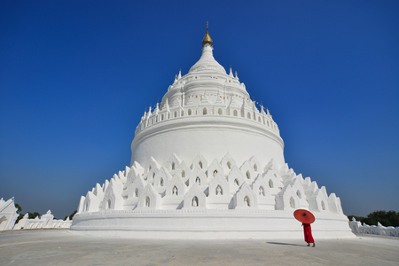 A Buddhist novice monk walking around the white stupa in sunny day.の写真素材