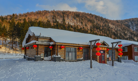 Harbin, China - Feb 24, 2018. Wooden houses covered by snow with red lanterns at mountain town in Harbin, China.のeditorial素材
