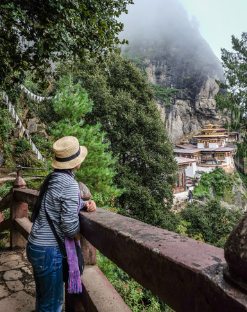 A woman looking at the Taktsang Palphug Monastery (Tiger Nest) on misty mountain in Paro, Bhutan.のeditorial素材
