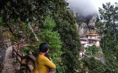 A woman looking at the Taktsang Palphug Monastery (Tiger Nest) on misty mountain in Paro, Bhutan.のeditorial素材