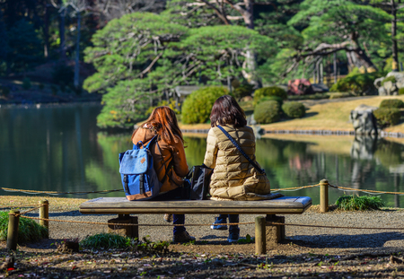 Young woman sitting on wooden bench at city park in sunny day.の写真素材