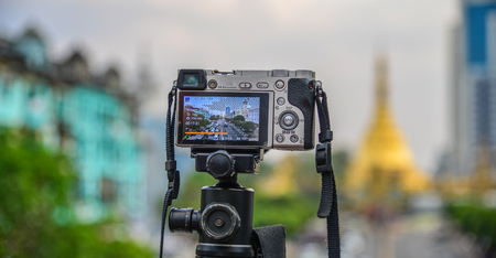 Digital camera on tripod with Yangon cityscape background.