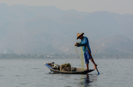 Inle, Myanmar - Feb 14, 2016. Burmese man using the unique methods of rowing and catching fish on Inle Lake. Inle is one of the highest lake at an elevation of 880m.のeditorial素材