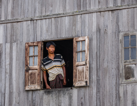 Inle, Myanmar - Feb 15, 2016. A man standing at thÆ° window of wooden house on Inle Lake, Myanmar.のeditorial素材